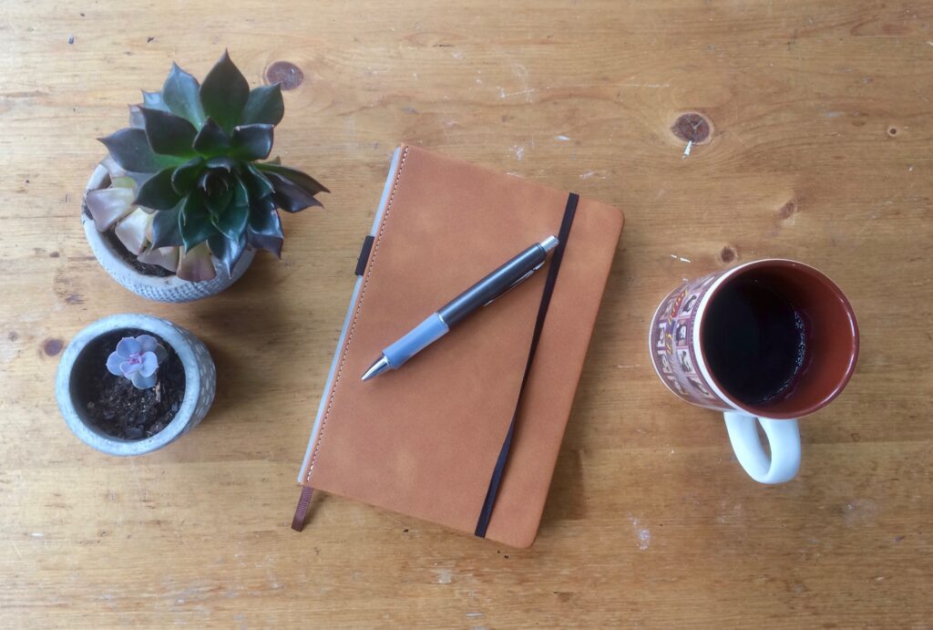 Best notebook for writing with pen, coffee mug and plants on a table top.